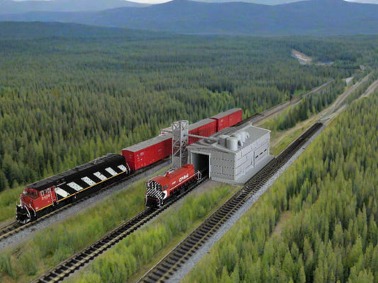 A model train set featuring a timber plant building with red train cars alongside. The scene is set in a forested area with mountains in the background.