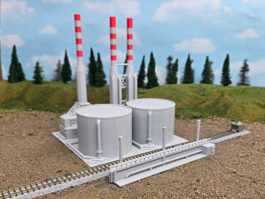 Z scale model of an oil refinery with two large oil tanks, pipe work, a cracker unit, two flare stacks, and a catwalk, set on a train track.
