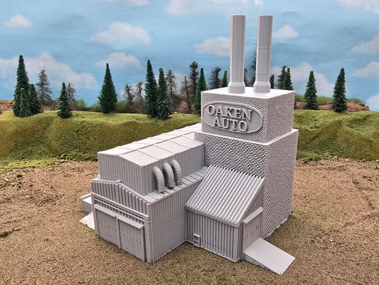Z scale model of an auto factory with textured brick walls, steel corrugated factory walls, loading ramps, chimney stacks, and a loading/unloading dock.