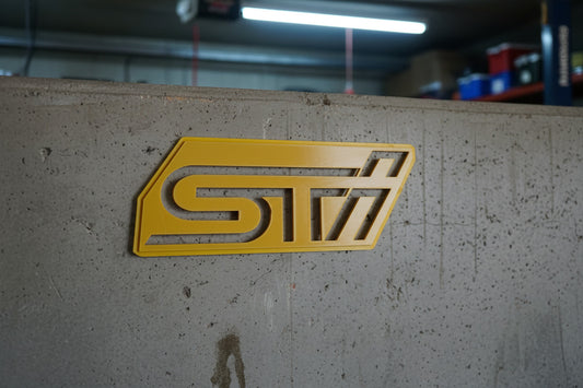 Yellow and white 'STI' logo on a textured surface with a light gray background