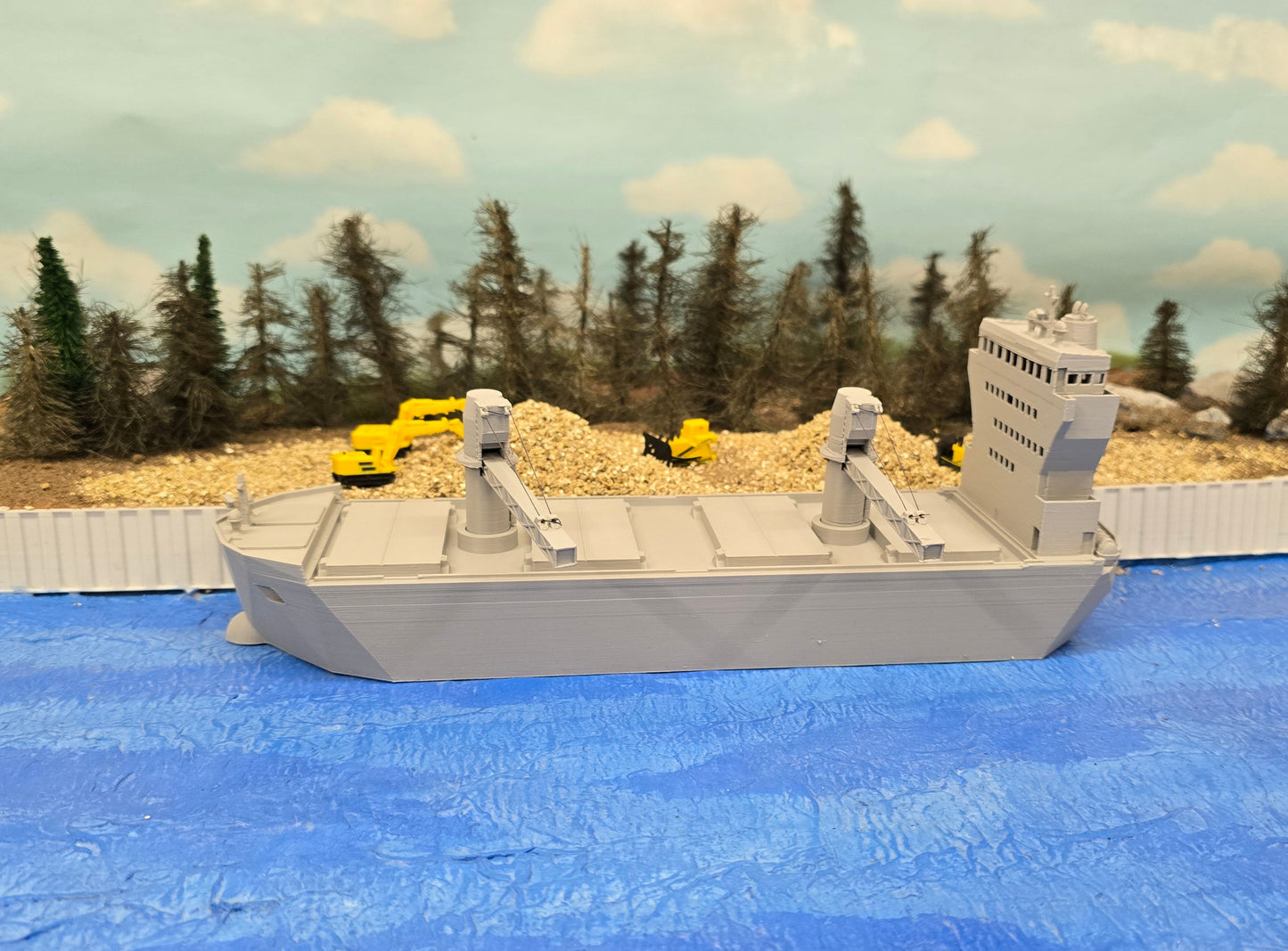 Model ship on a blue surface with trees and mountains in the background
