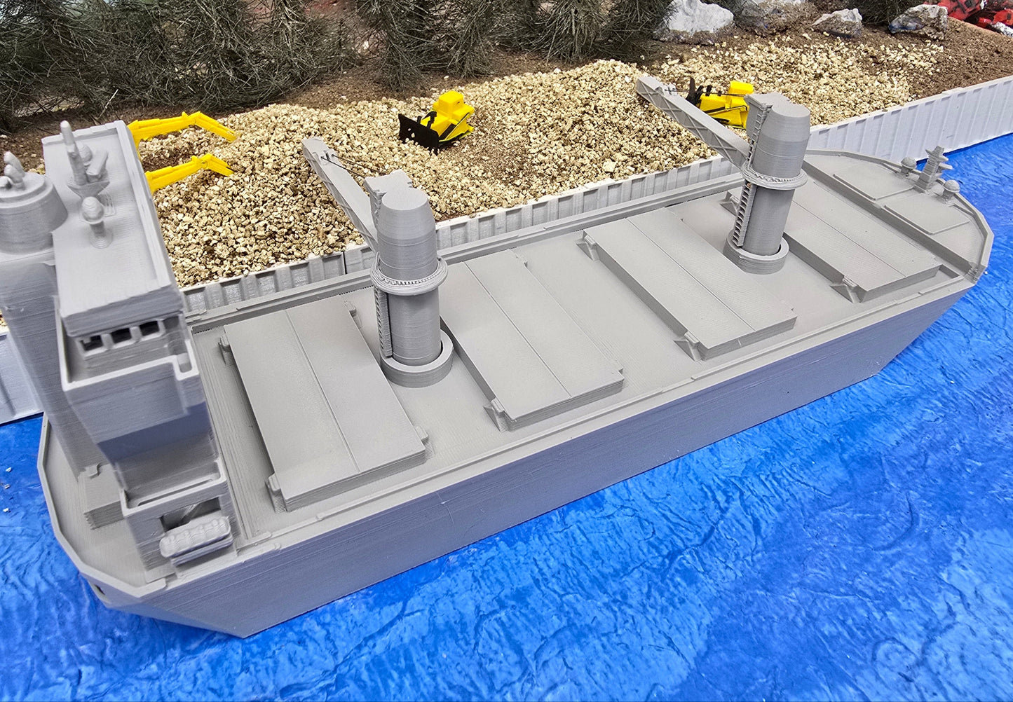 Model cargo ship on a blue surface with a forest background