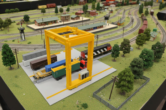 Model of a n scale train yard with a yellow crane and toy trains on a train table.