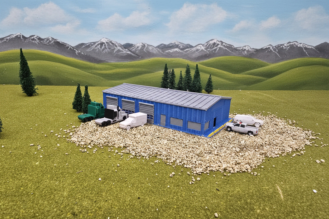 Model of a blue building with vehicles on a grassy area with trees and rocks in the background.