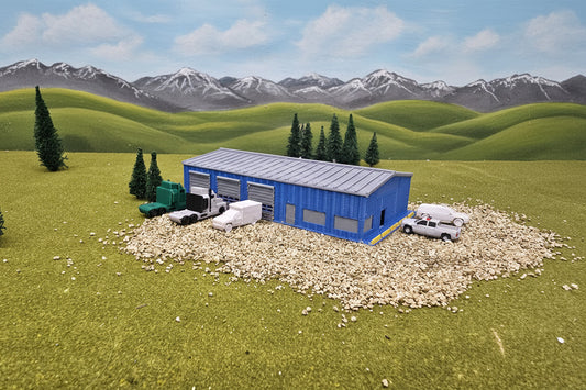 Model of a blue building with vehicles on a grassy area with trees and rocks in the background.