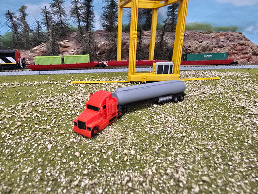 Model red truck with gray tanker on a grassy area with a yellow structure in the background.
