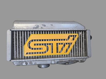 Radiator with a yellow 'STI' logo on a concrete floor