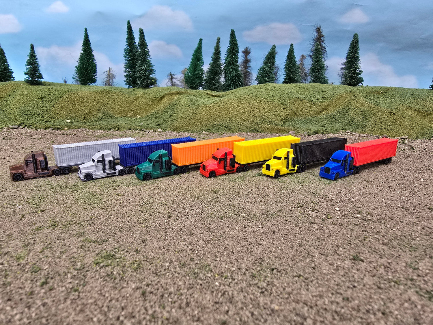 Colorful model trucks on a dirt surface with green trees in the background