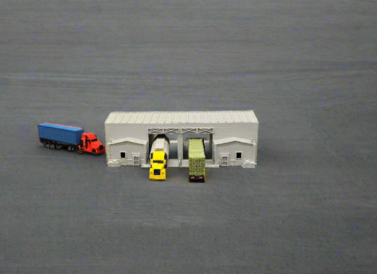 Model train set with a small building, trees, and model cars on a grassy area.