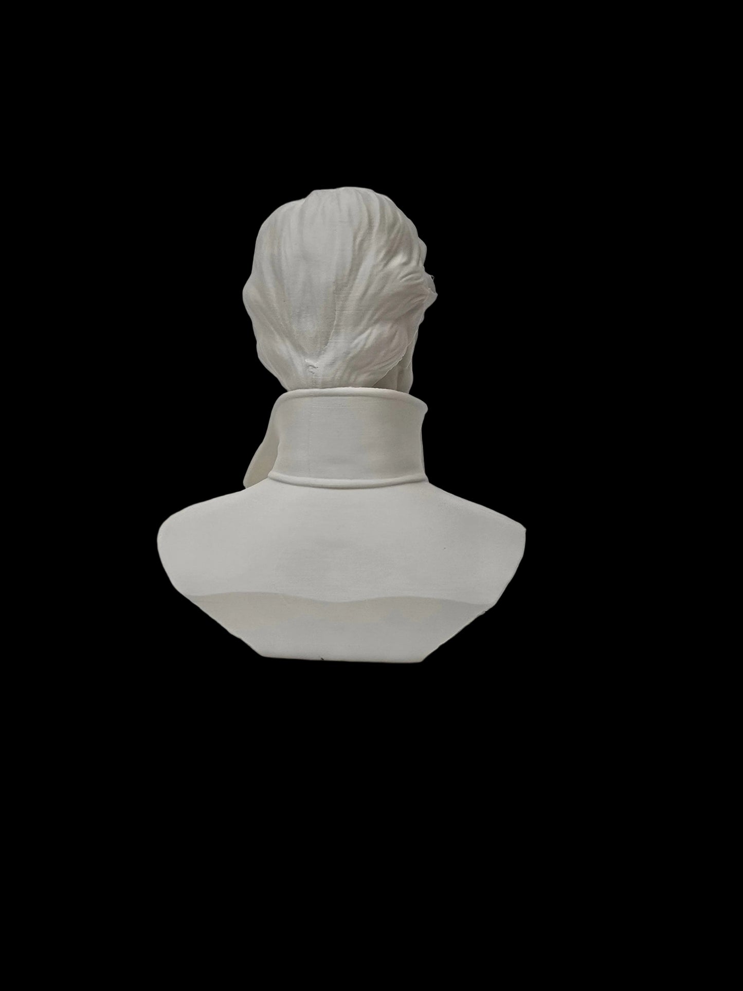 A white ceramic or porcelain bust sculpture of a classical figure viewed from the back, set against a textured white wall and surface.