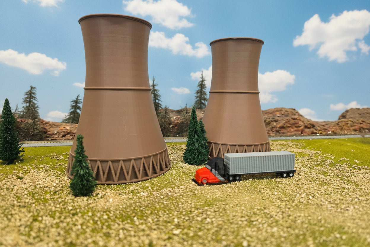 Model of cooling towers with a small model truck in front, set against a scenic background.