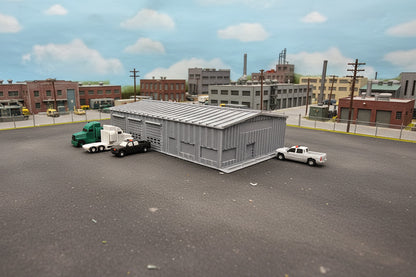 Model of a storage building with trucks and a car on a grassy field
