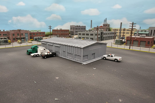 Model of a storage building with trucks and a car on a grassy field