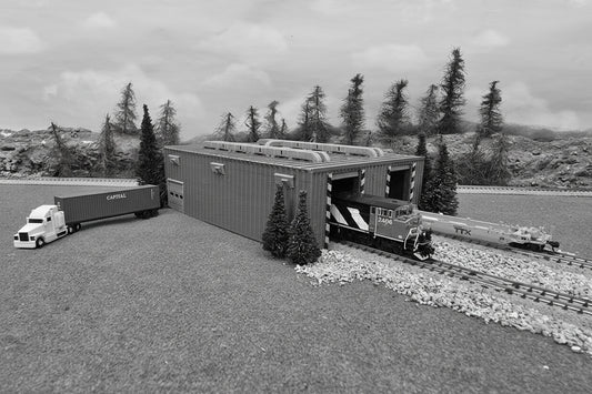 Model train set with blue cargo container, green truck, and trees in the background